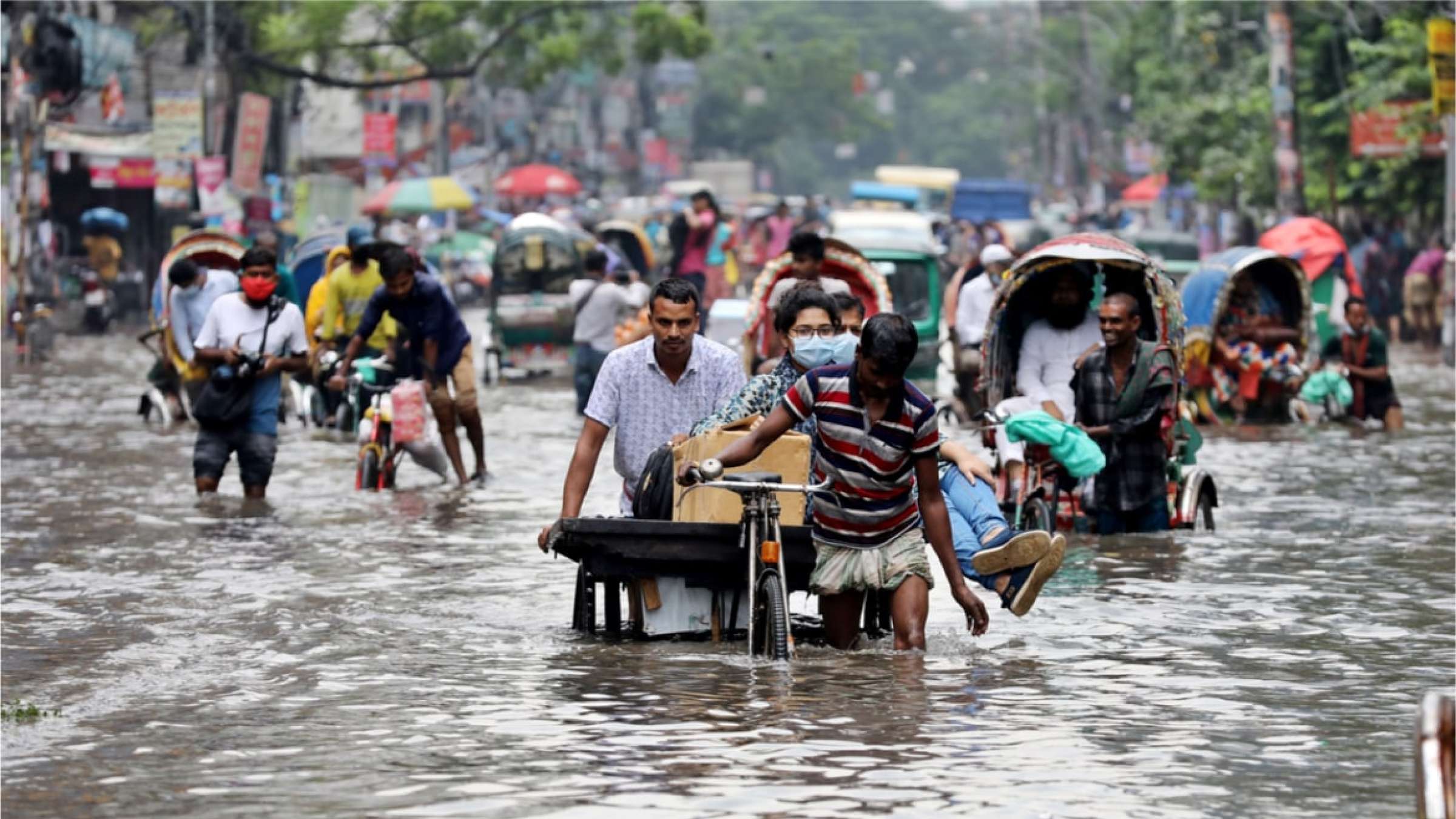 2020年，Riksha司机走在孟加拉国被洪水淹没的街道上。