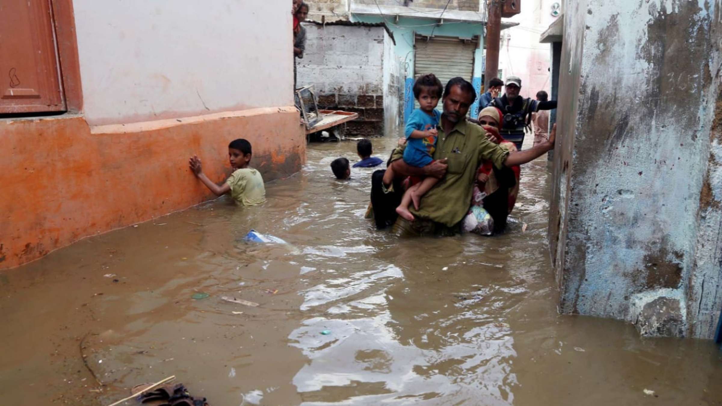 在巴基斯坦，成年人和孩子走在被洪水淹没的街道上