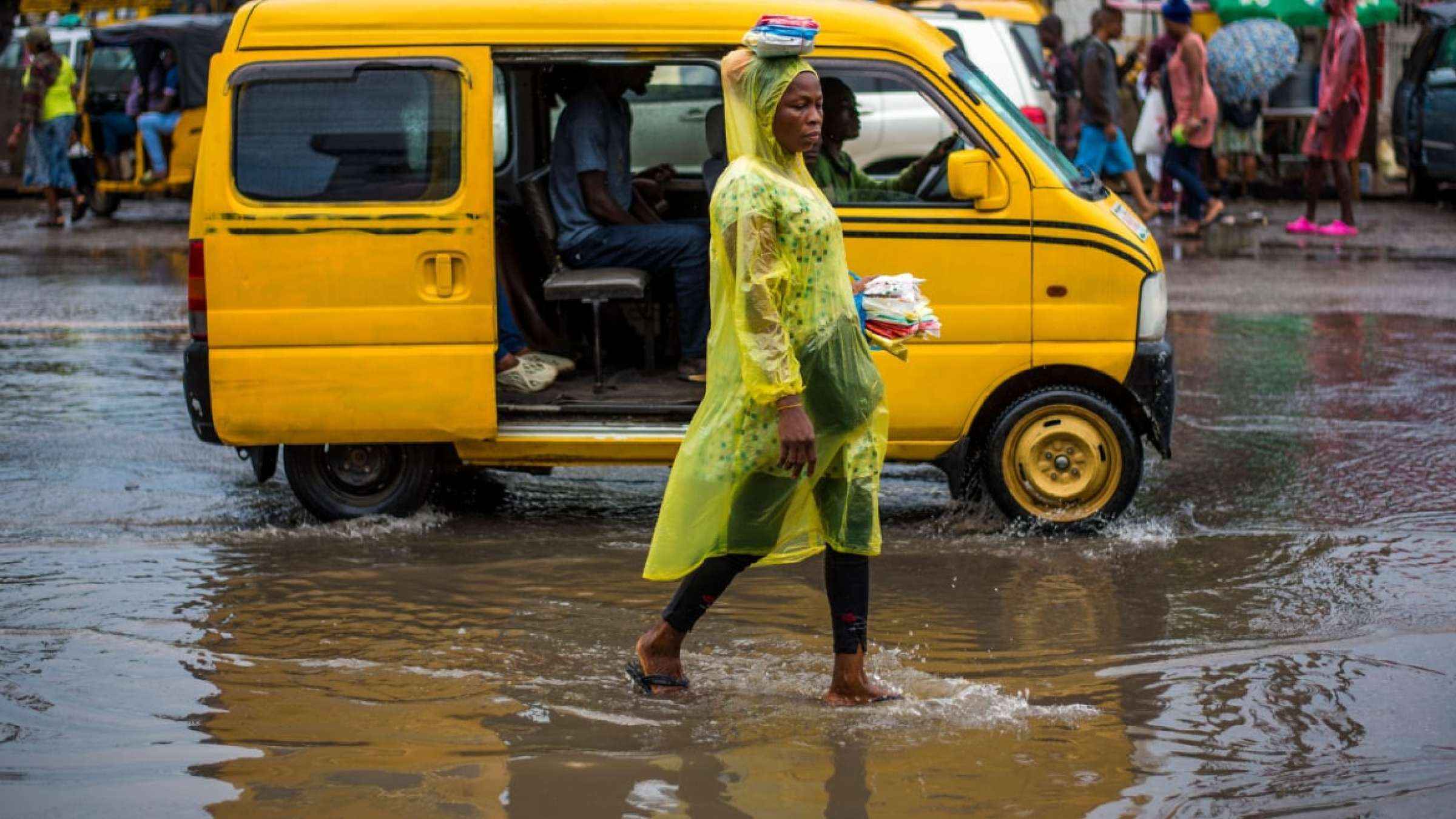 尼日利亚一名女子走在被洪水淹没的街道上，头上披着一件黄色的防雨斗篷。