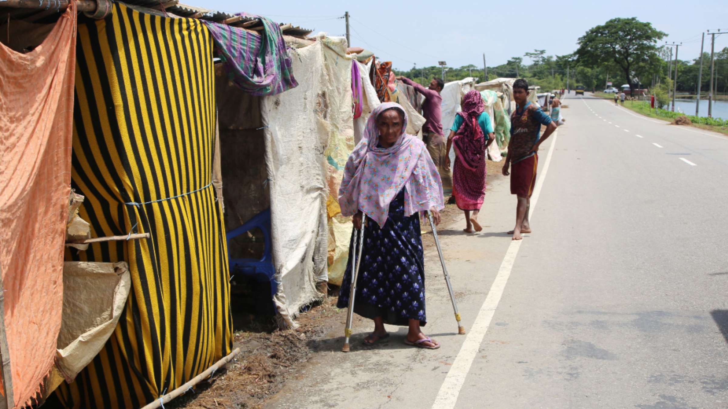 2022年，孟加拉国，一名受洪水影响的残疾老妇站在临时避难所前